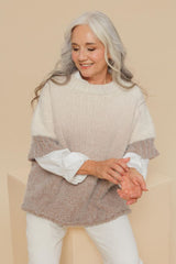 Círculo Marfim – Acrylic Gradient Cake Yarn (400 m / 200 g) - A smiling older woman with long silver-gray hair models a textured knit sweater with a color-blocked design. The top is a warm cream-beige, the middle band is taupe-brown, and the sleeves are white.