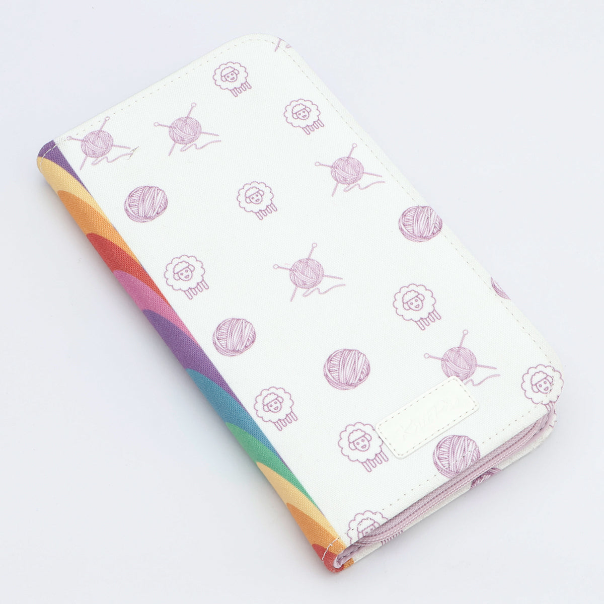 KnitPro Symfonie 2 double pointed needle set, 20 cm - A zippered wallet or planner cover with a white background decorated with light purple yarn and sheep illustrations, featuring a vibrant rainbow-colored striped spine.