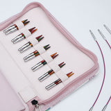 KnitPro Symfonie 2 Mini interchangeable needle set, 5 cm - A pink zippered carrying case holding multiple knitting needles arranged in elastic loops. The needles have silver metal shafts and tips with multicolored yarn wrapped around them.