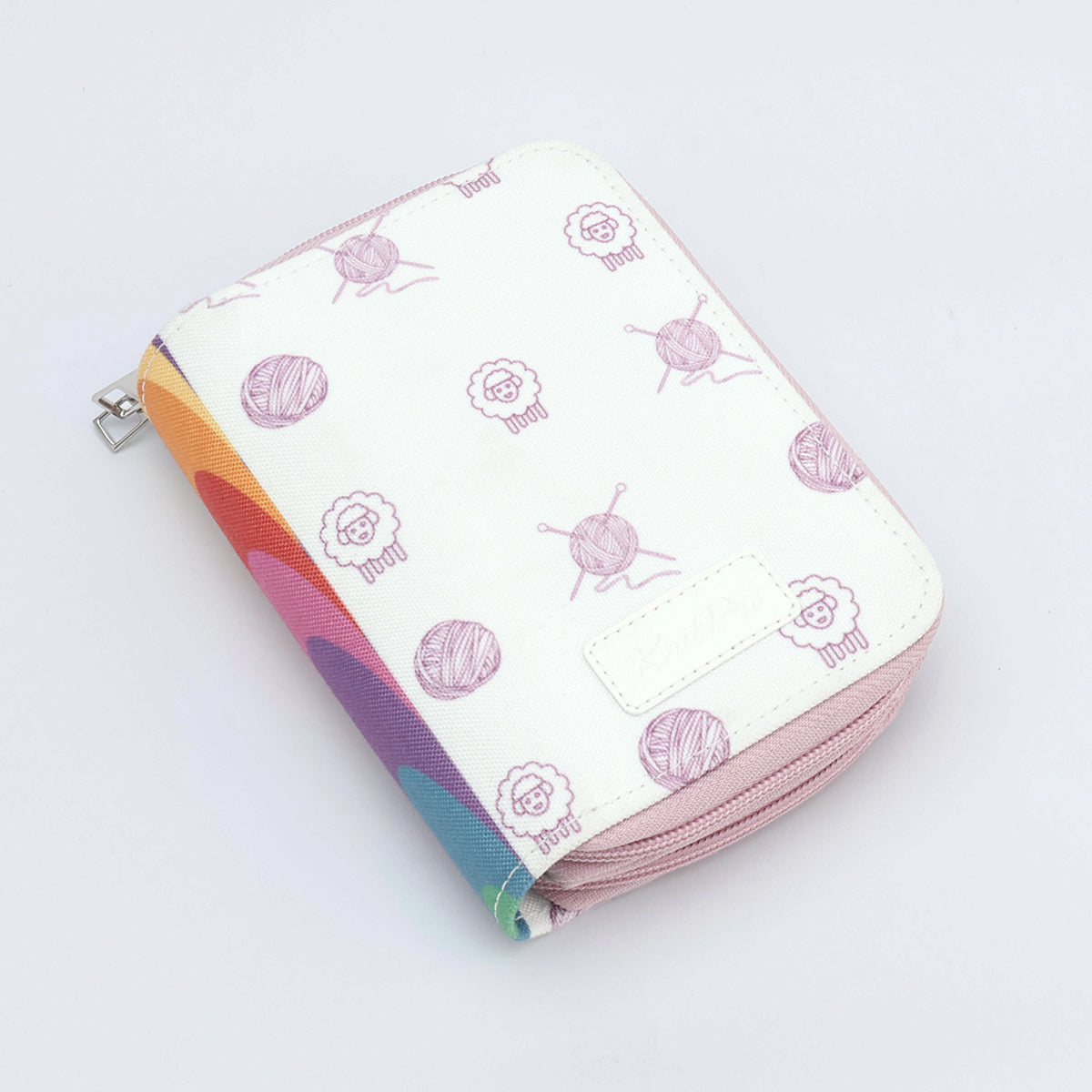 KnitPro Symfonie 2 Normal interchangeable needle set, 13 cm, Chunky - A zippered wallet or organizer case with a white exterior printed with pink yarn-ball and knitting-needle motifs, plus a multicolor striped side panel in orange, pink, purple, teal, and green. It is photographed on a clean white background.